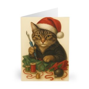 Festive sewing Christmas card with adorable tabby cat wearing a Santa hat, holding a seam ripper, surrounded by thread, holly and ornaments — cosy holiday card for sewing lovers | by T Larkin.